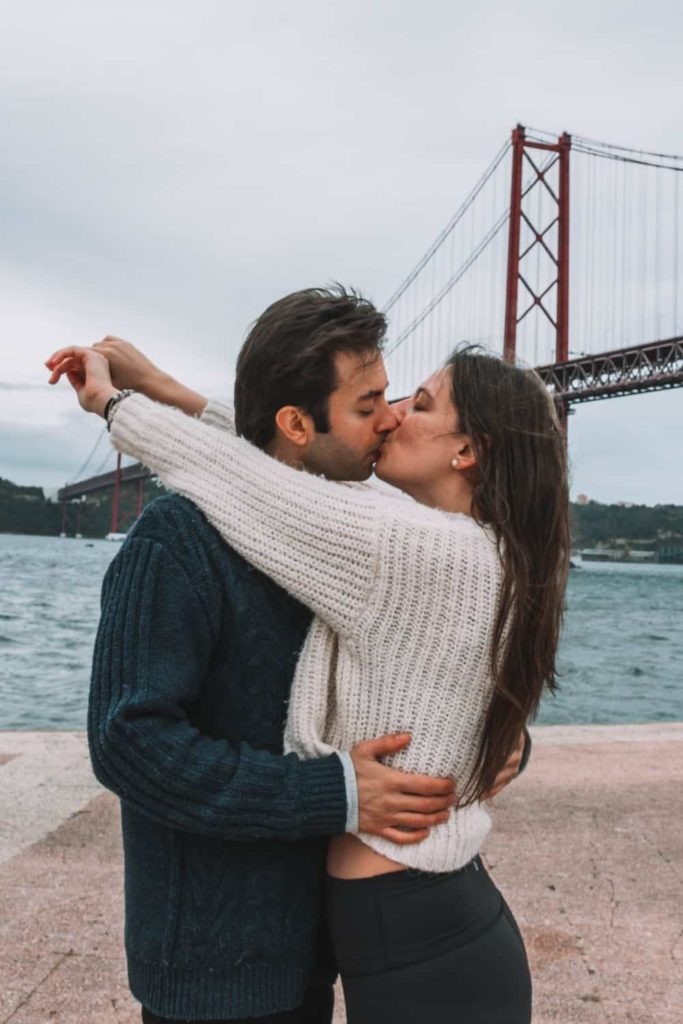 couple in front of Ponte 25 de Abril in Lisbon, which looks like Lisbon Golden Gate Bridge