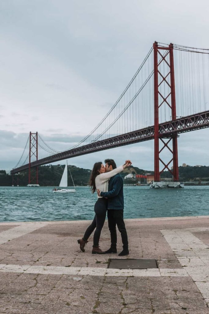 couple in front of Ponte 25 de Abril in Lisbon, which looks like Lisbon Golden Gate Bridge
