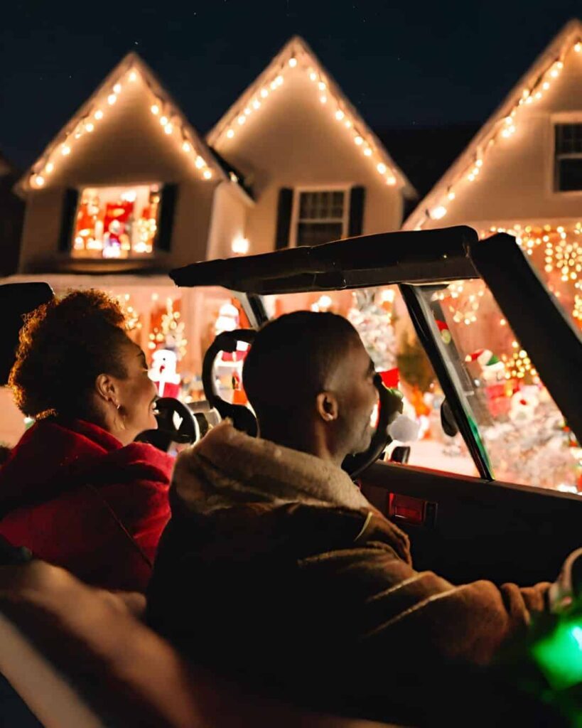 couple driving by house decorated with Christmas lights