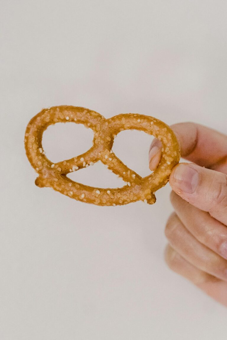 Closeup shot of delicious baked pretzels with salty specks placed in fingers on gray background