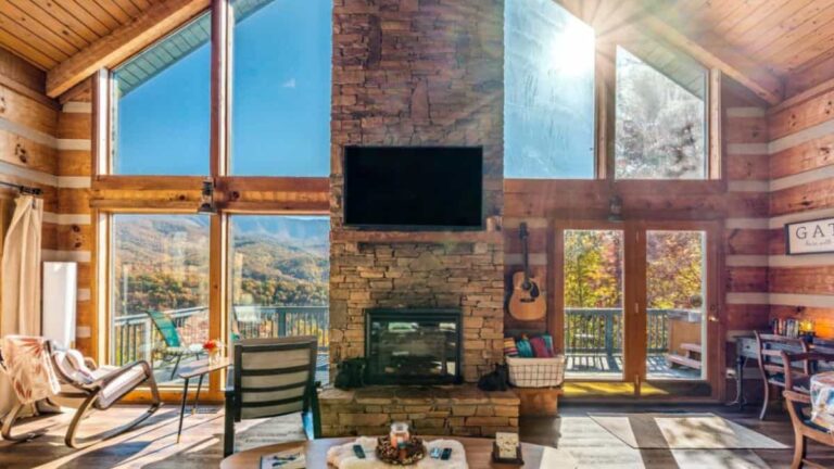 A frame cabin with large windows and tv mounted on stone fireplace