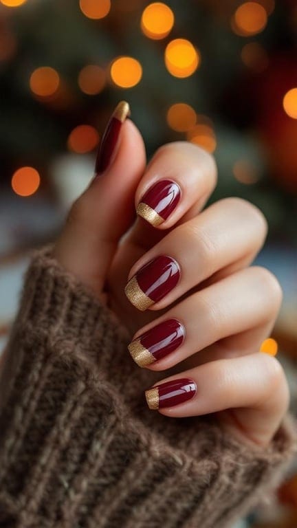 Close-up of hands with gold and burgundy diagonal French tip nails, wearing a cozy sweater.