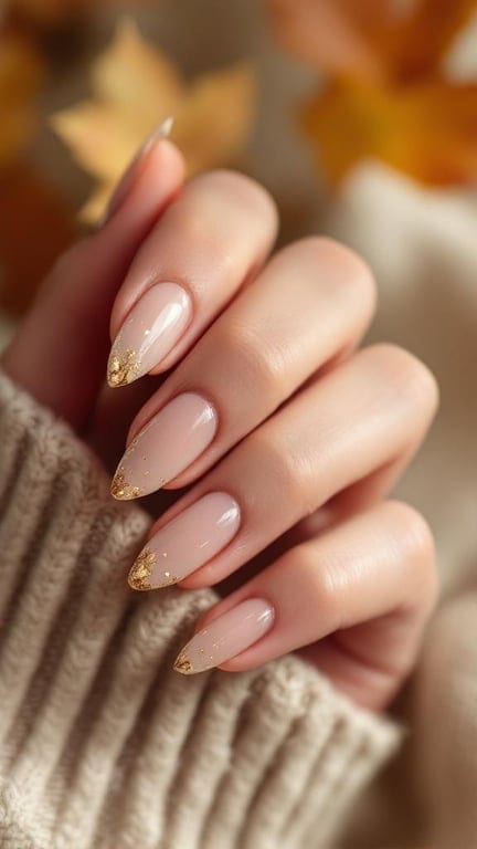 Nude nails with gold leaf accents, showcasing a stylish and festive design.