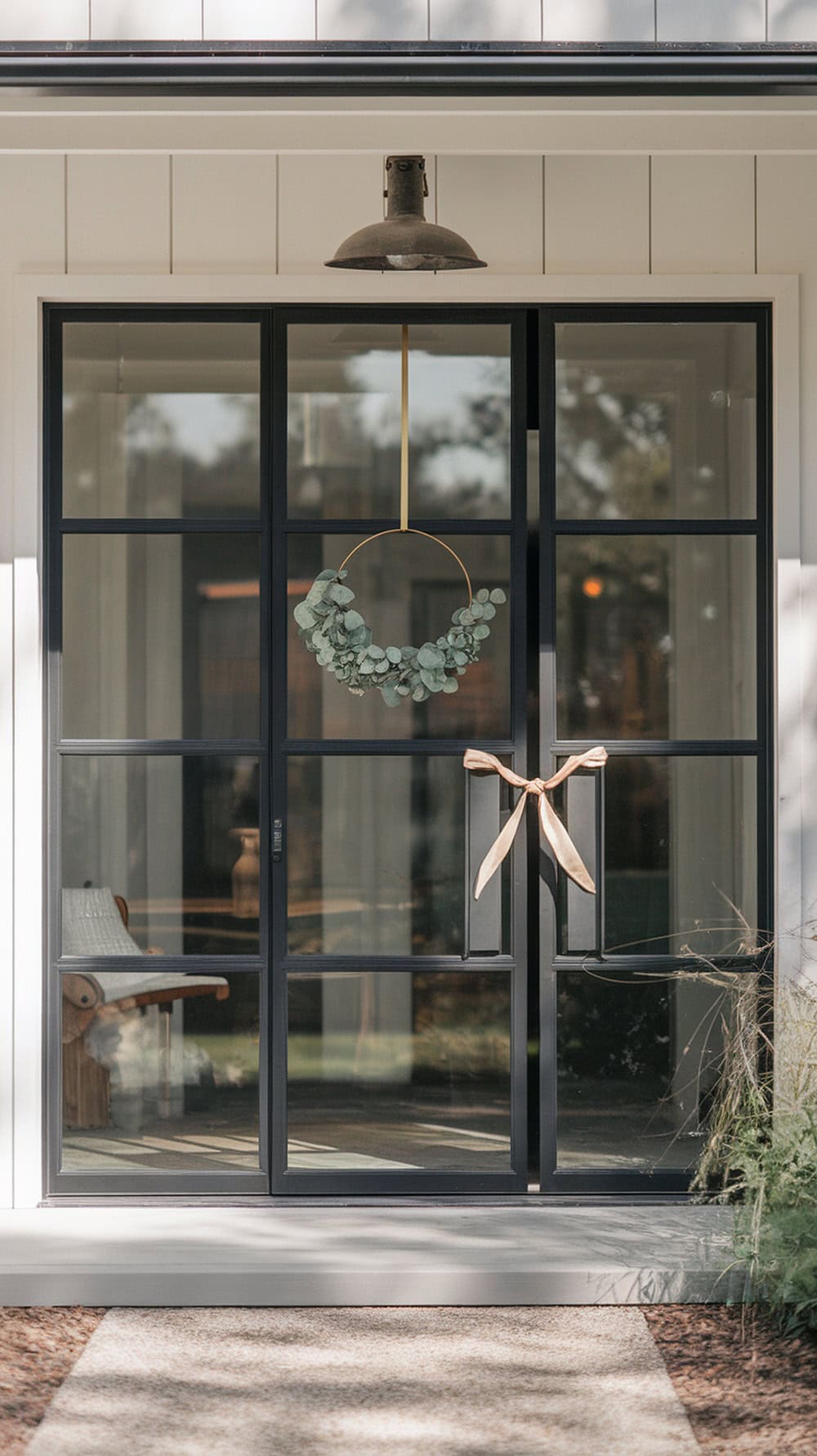 A minimal green wreath with gold hoops hanging on a modern farmhouse front door.
