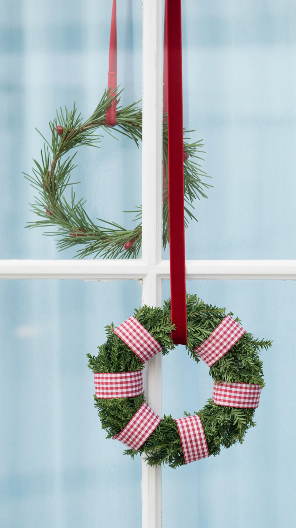 Two layered wreaths in red and white hanging in a window, showcasing a modern farmhouse decor style.