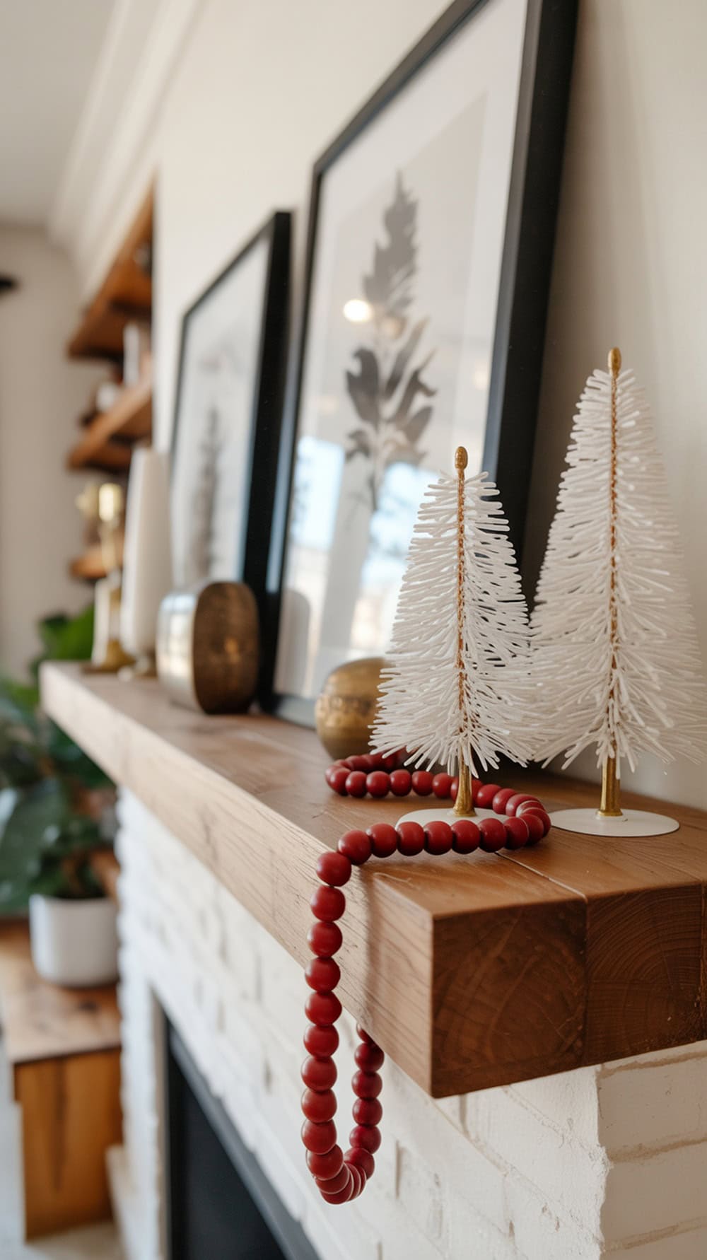 A modern farmhouse mantel decorated with white trees and red beads.