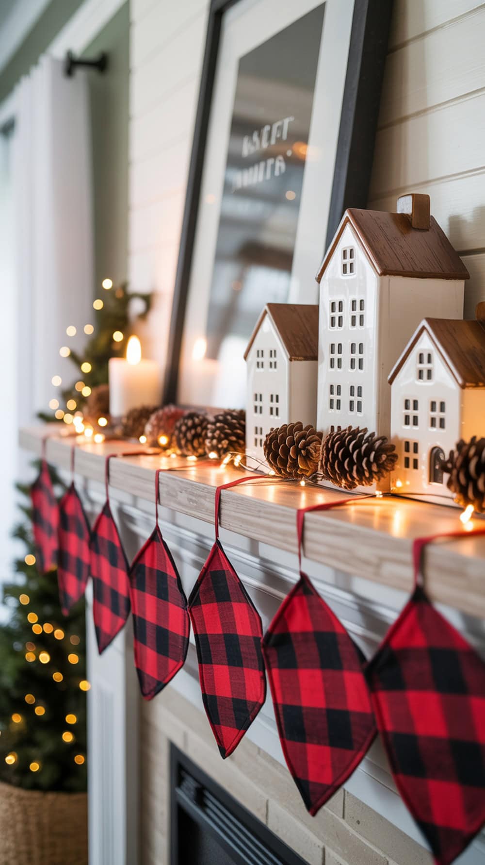 A cozy fireplace mantel decorated with a red checked garland, white houses, pinecones, and fairy lights.