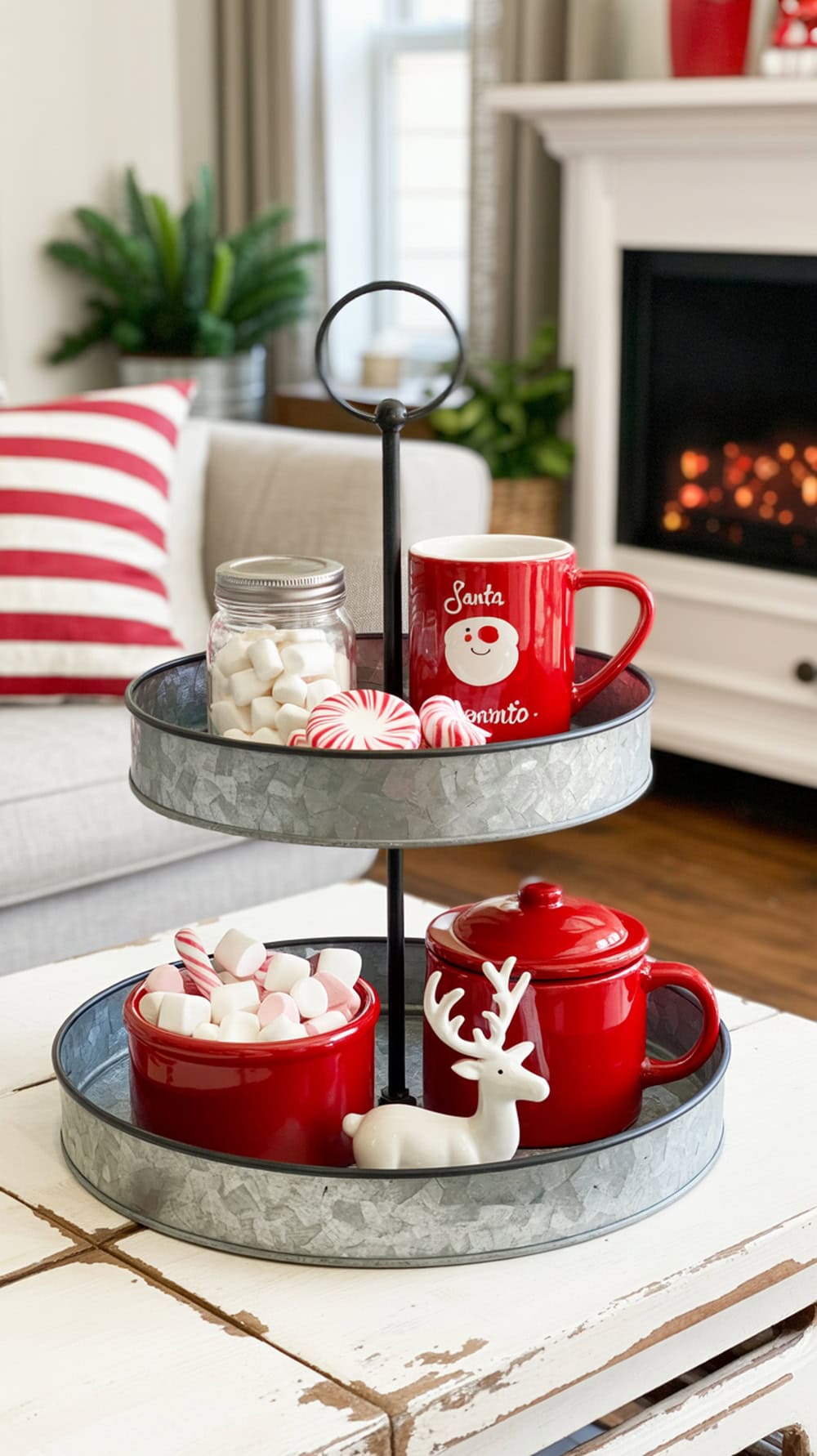 A tiered tray decorated with red and white Christmas items, including a Santa mug, marshmallows, peppermint candies, and a white reindeer figurine.