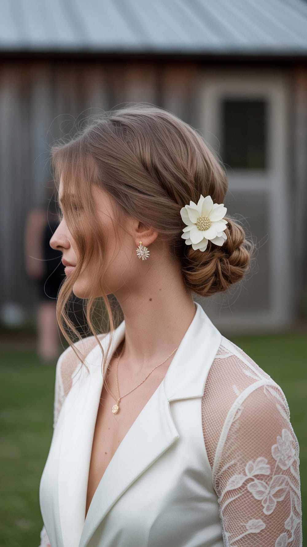 A woman with long wavy hair styled in a messy side bun adorned with a floral pin, wearing a white outfit.