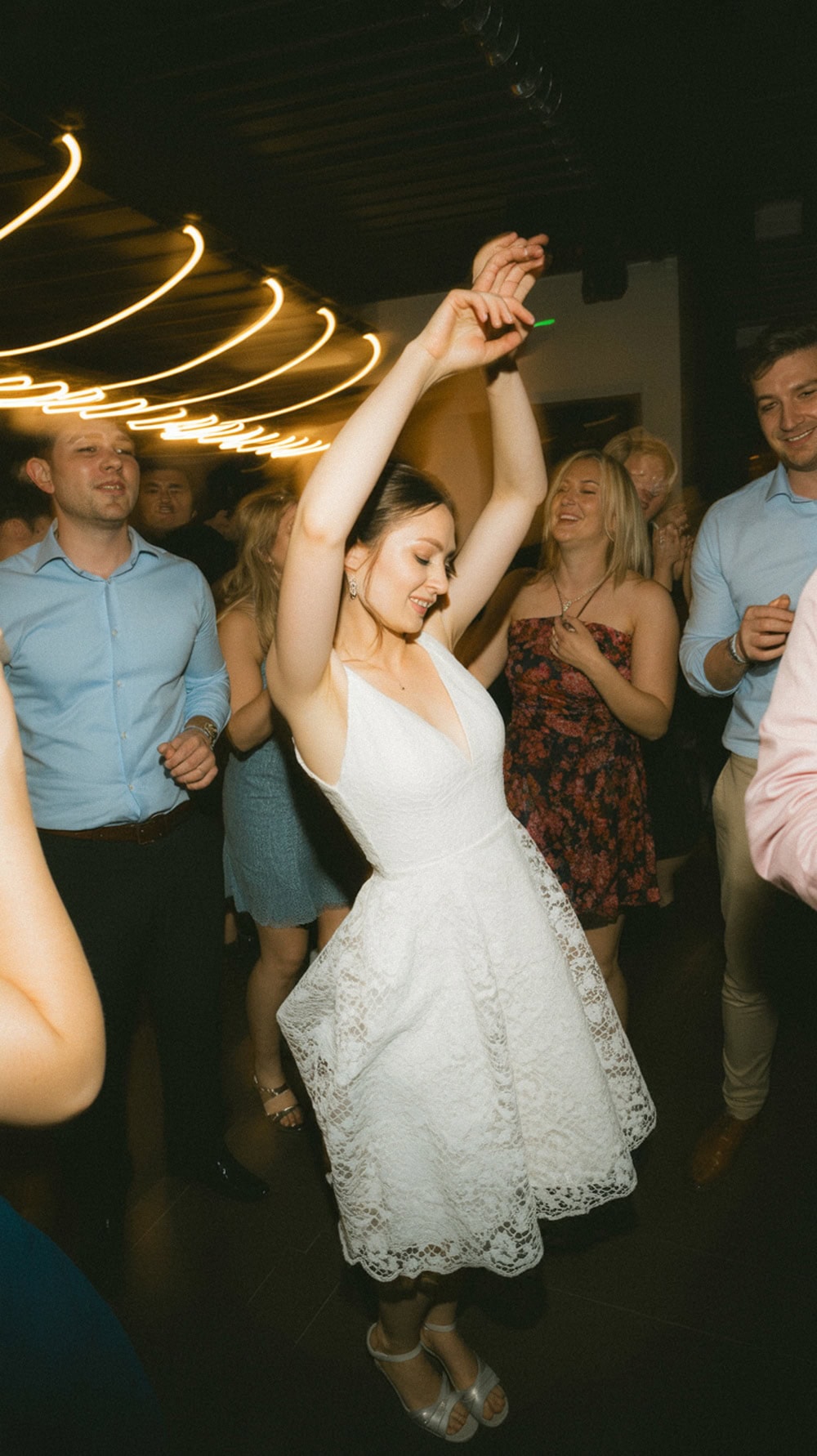 A woman dancing joyfully in a white dress at a wedding reception.