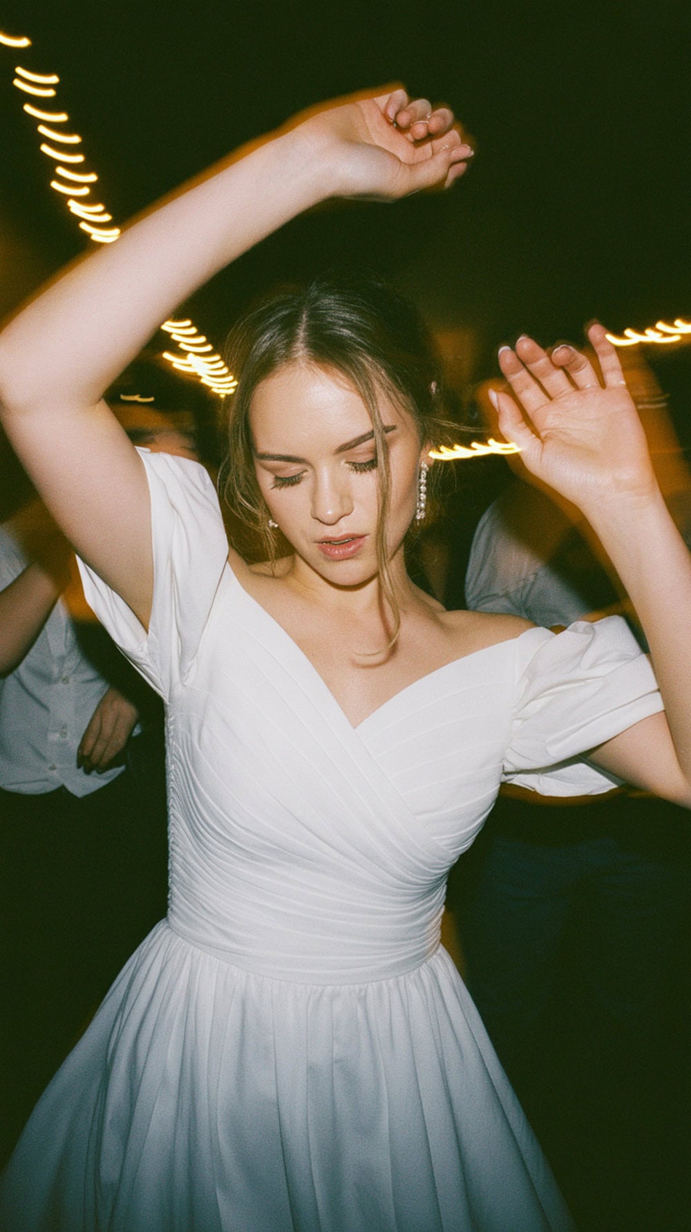 A bride dancing in a white wedding dress with off-the-shoulder sleeves.