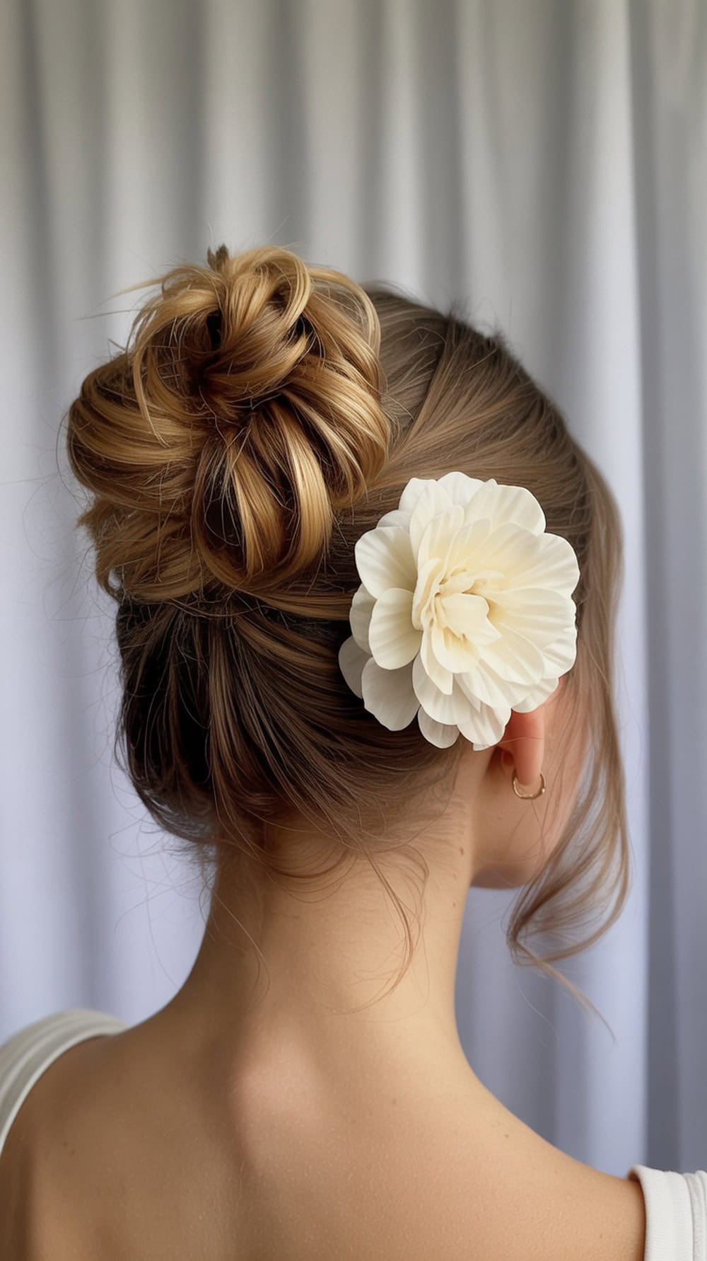 A woman with a braided bun hairstyle adorned with a floral clip, showcasing loose curls framing her face.
