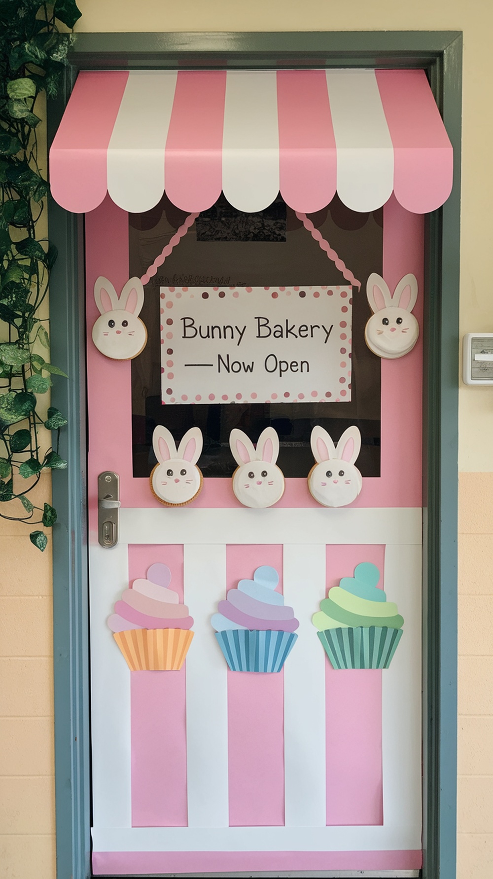 A classroom door decorated with a pink bakery theme featuring bunnies and cupcakes.