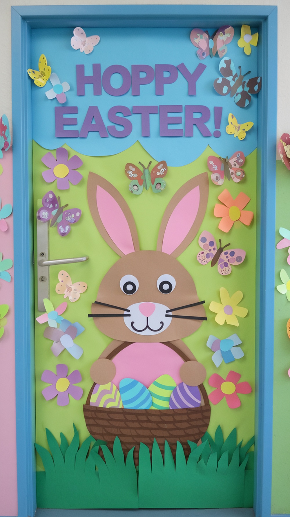 A classroom door decorated with a bunny holding a basket of eggs, surrounded by flowers and butterflies, with the words 'Hoppy Easter!'