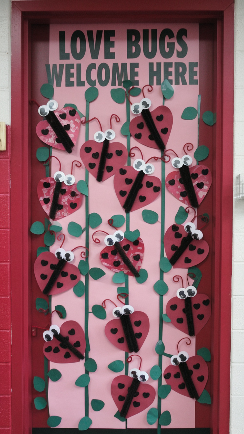 Classroom door decorated with love bugs made from heart shapes, with green leaves and a welcoming message.