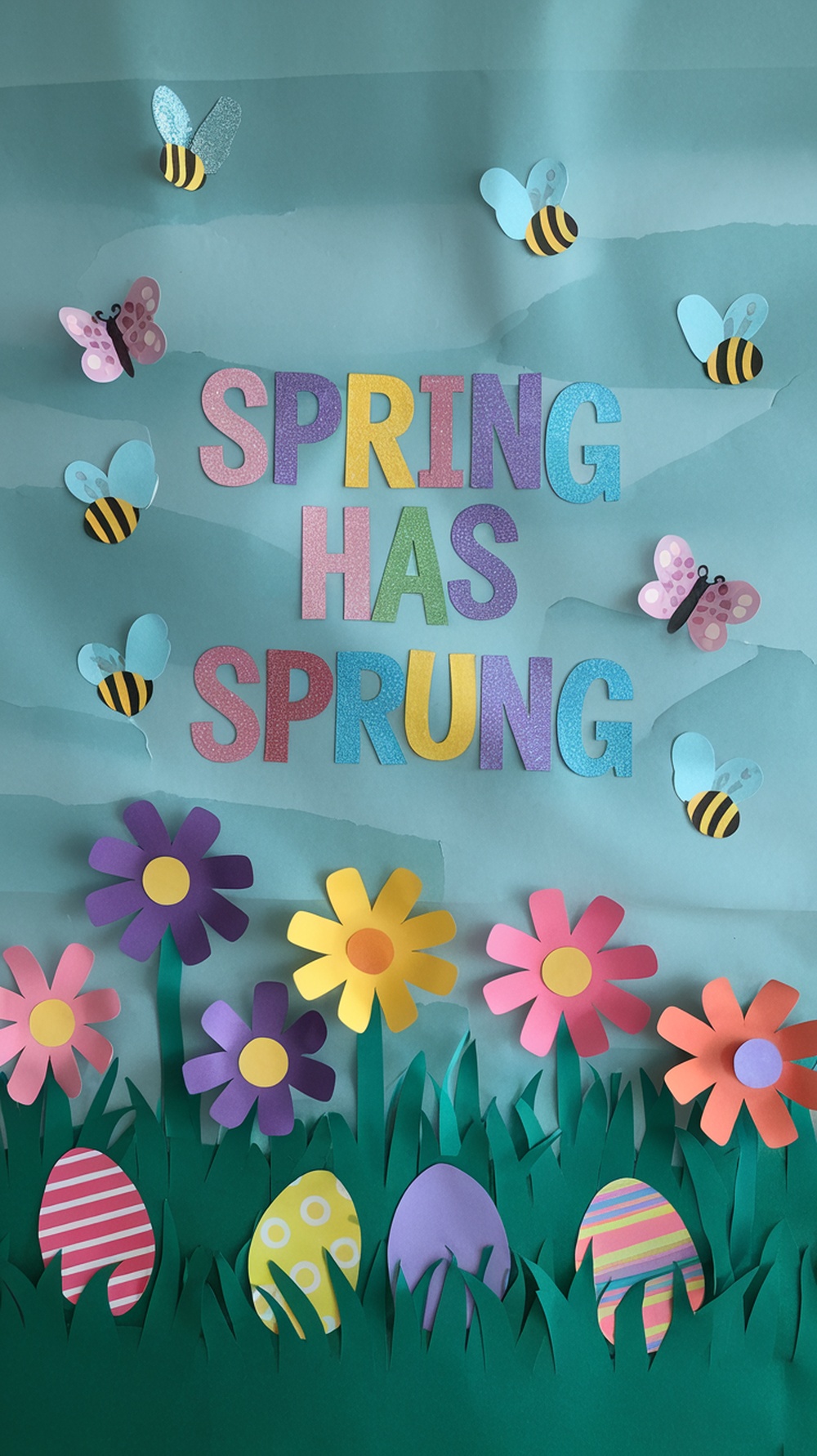 Colorful spring-themed classroom door decoration with flowers, butterflies, and Easter eggs.