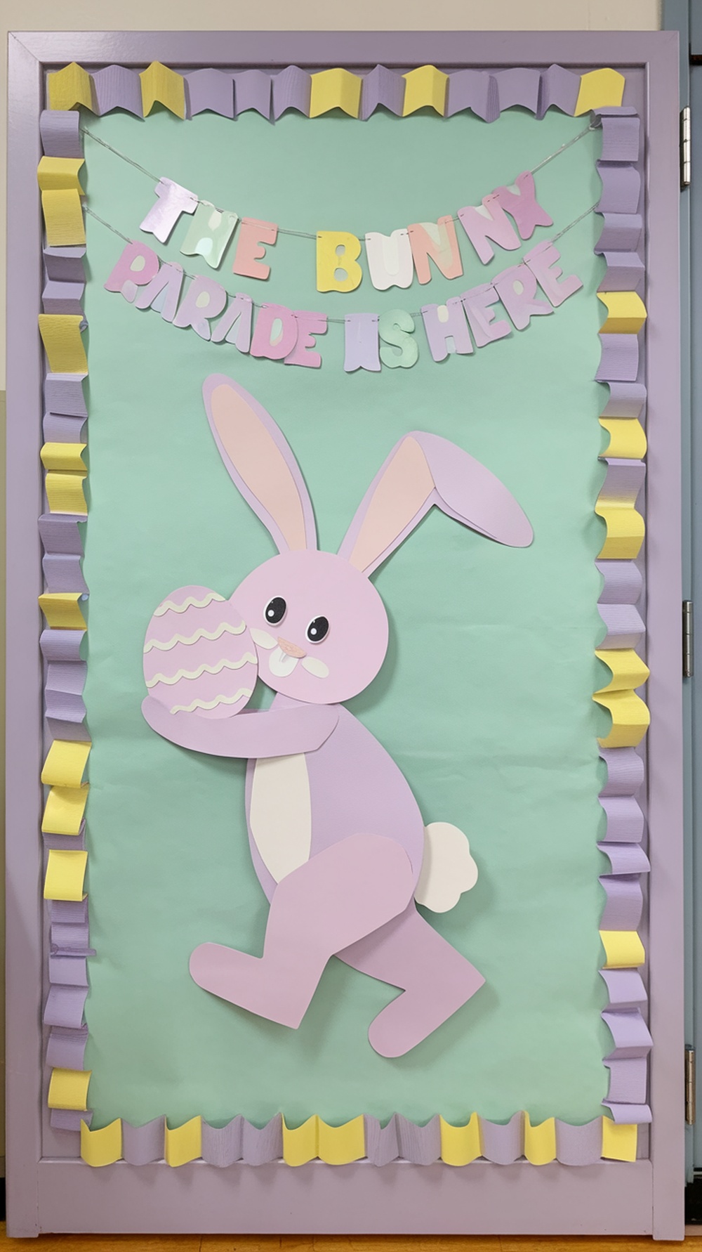 A classroom door decorated for Easter with a bunny and colorful banner.