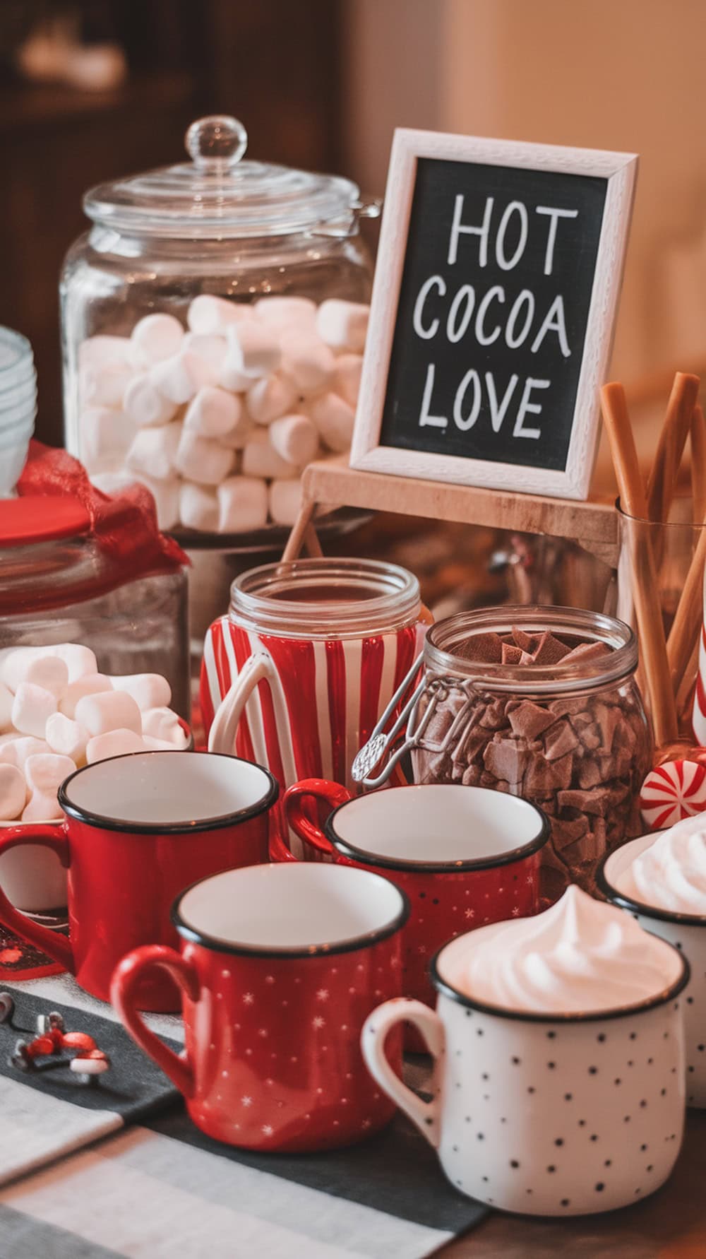 A cozy hot chocolate bar setup with mugs, marshmallows, chocolate toppings, and a sign that says 'Hot Cocoa Love'.