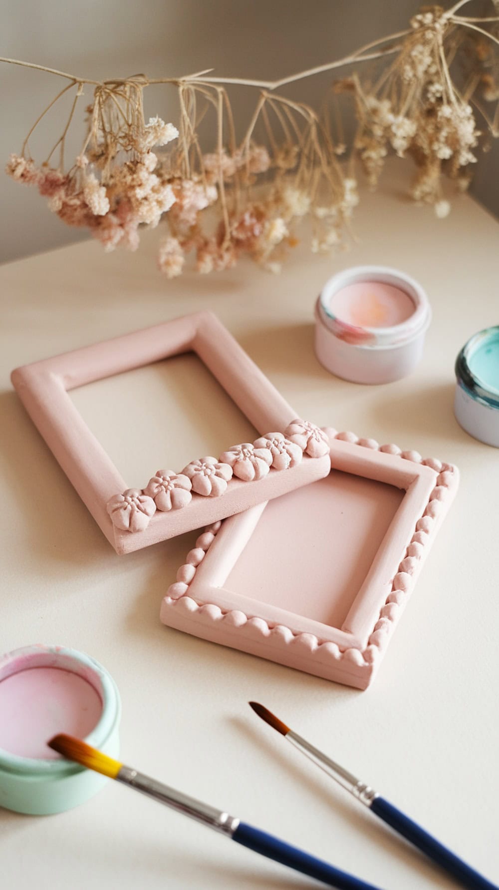 Two air dry clay picture frames with floral designs, paint, and brushes on a table.