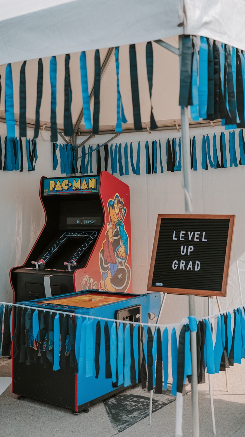 A backyard arcade tent featuring a Pac-Man arcade game, colorful streamers, and a sign that says 'Level Up Grad'.