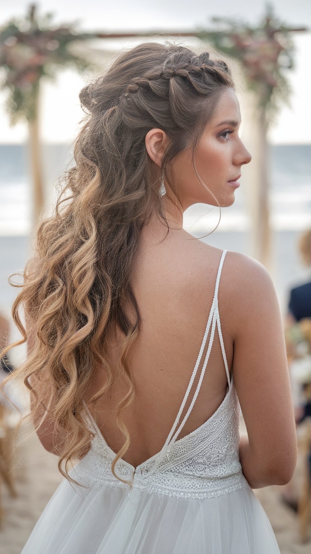 A woman with curly hair styled in a half-up, twisted layers and long curls, perfect for a beach wedding.
