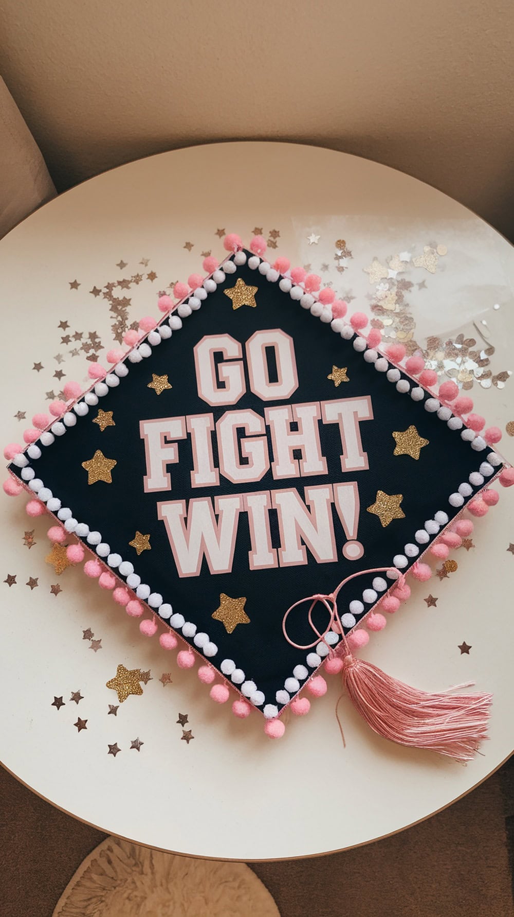 Graduation cap decorated with pom pom trim and a motivational cheerleading message.