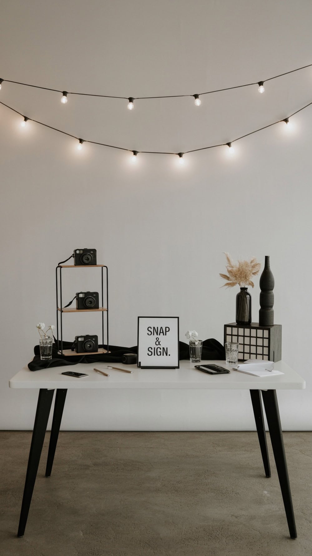 A stylish black and white photo booth table with cameras, a sign, and decorative elements.