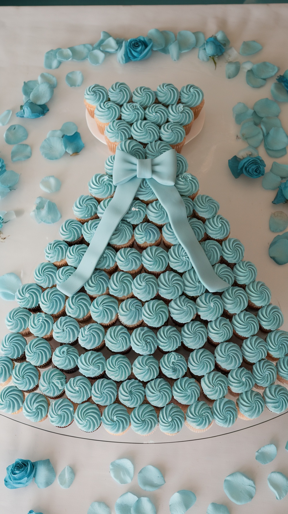 Cupcake display shaped like a blue dress with rose petals
