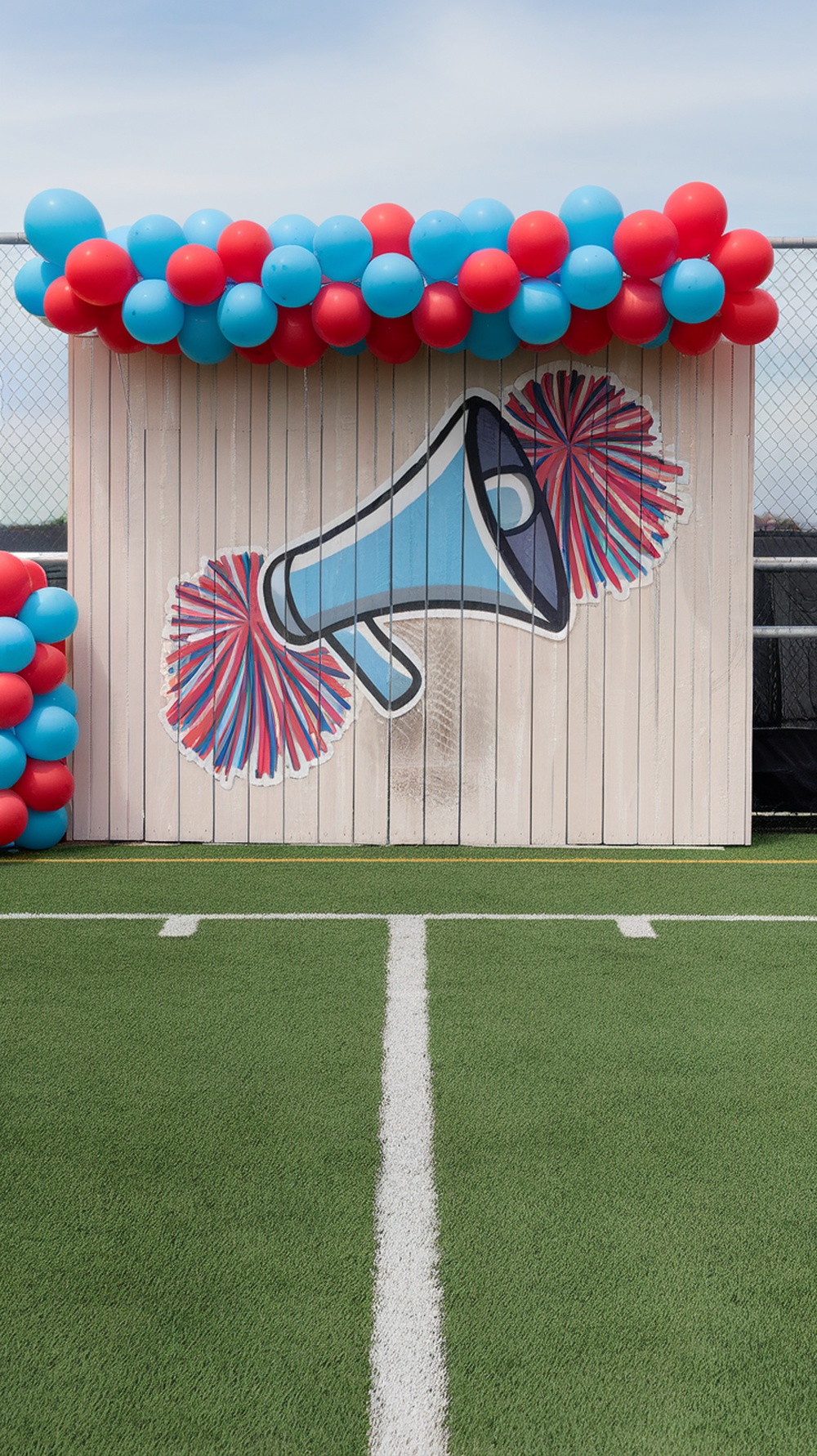 A colorful outdoor photo backdrop featuring a megaphone and pom-poms, decorated with red and blue balloons.