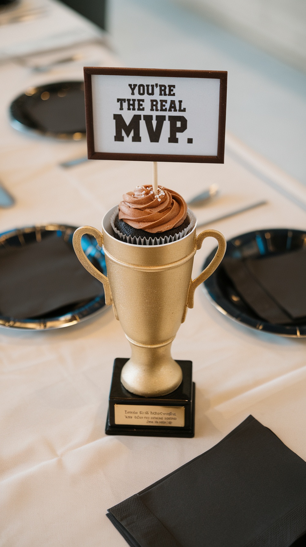 A golden trophy filled with a cupcake, topped with chocolate frosting and a sign that says 'You're the real MVP.'