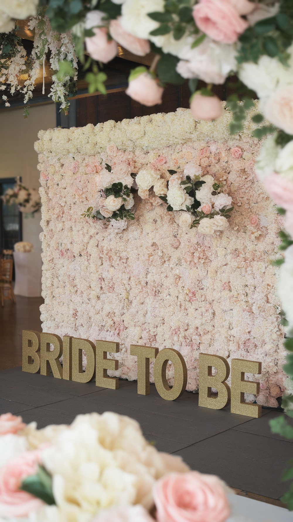 A flower wall backdrop for a bride-to-be party, featuring pastel flowers and golden letters spelling 'BRIDE TO BE'.