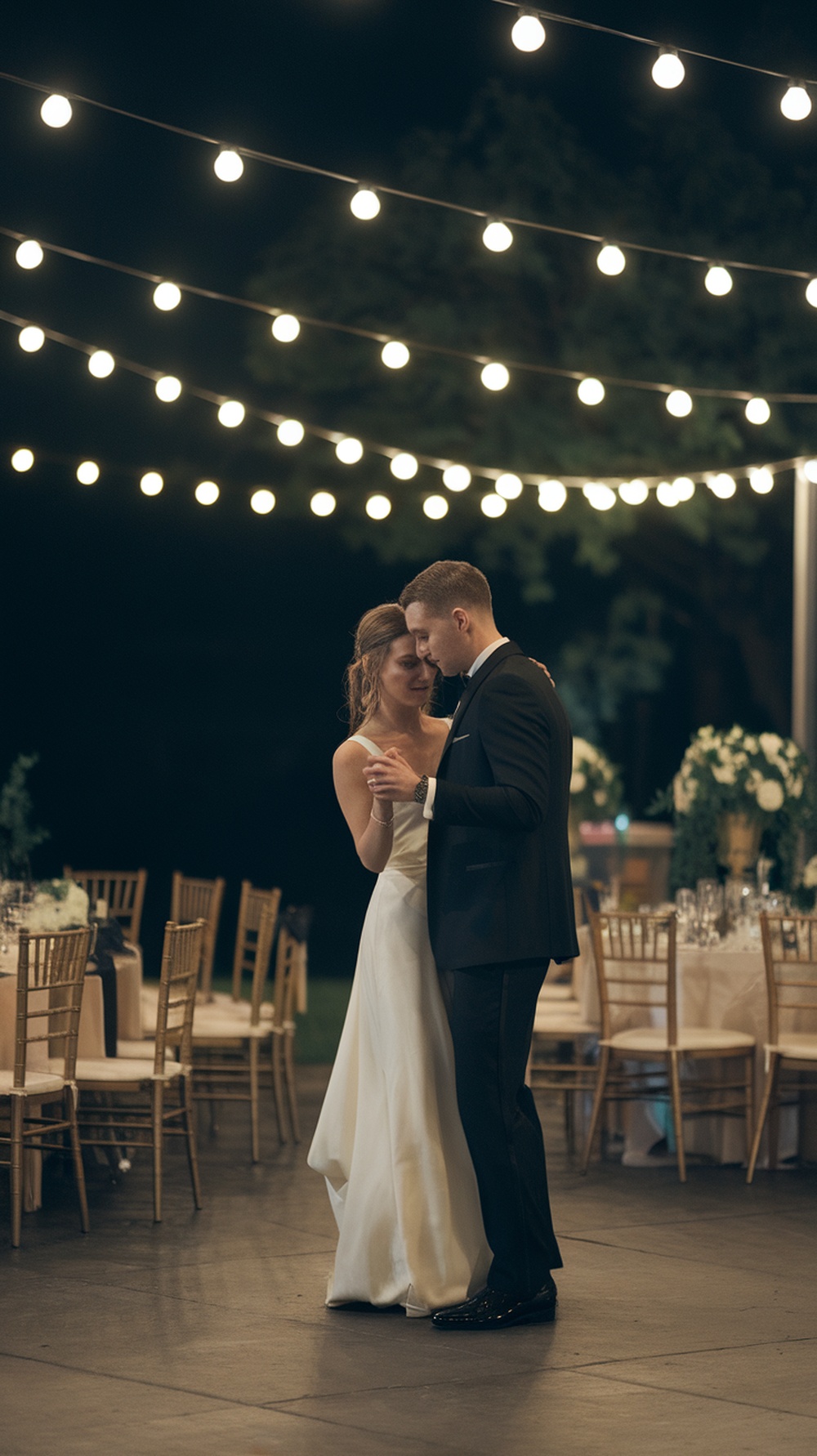 A couple enjoying a private last dance under string lights after their wedding reception.