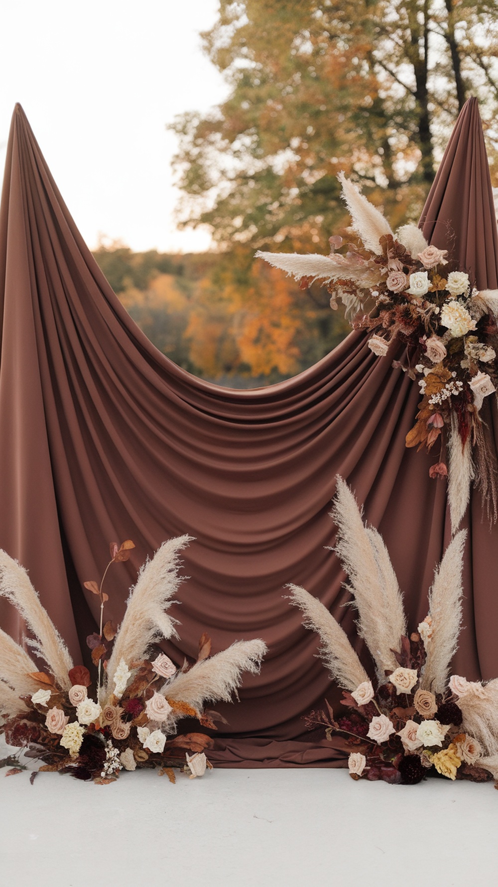 A chocolate brown draped backdrop decorated with dried flowers, featuring a warm fall atmosphere.