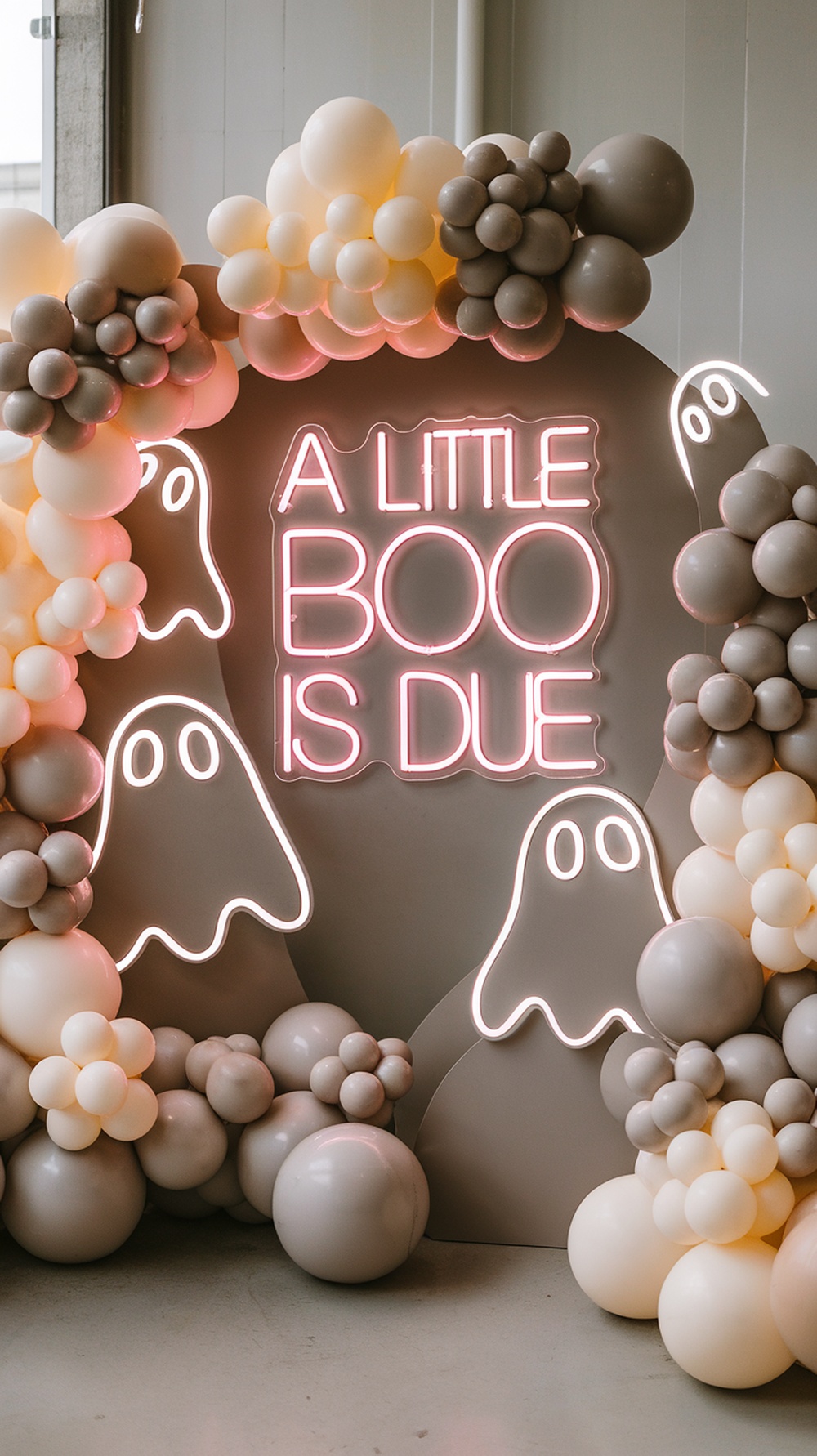 Spooky cute baby shower photo backdrop with balloons and a neon sign saying 'A Little Boo Is Due'.