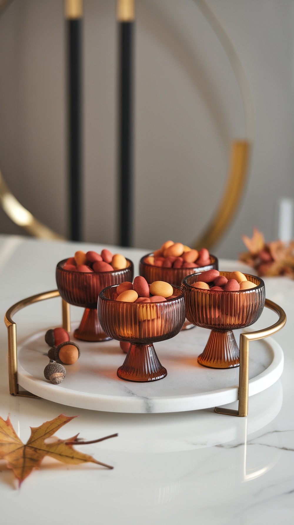 A marble tray with amber glass bowls filled with colorful candies, autumn leaves, and acorns arranged elegantly.